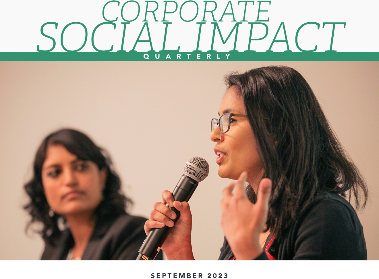 Corporate Social Impact Quarterly / September 2023. A woman with medium-dark skin and black hair speaking into a microphone while a second woman with medium-dark skin and black hair listens to her talk at Google’s Community Space.